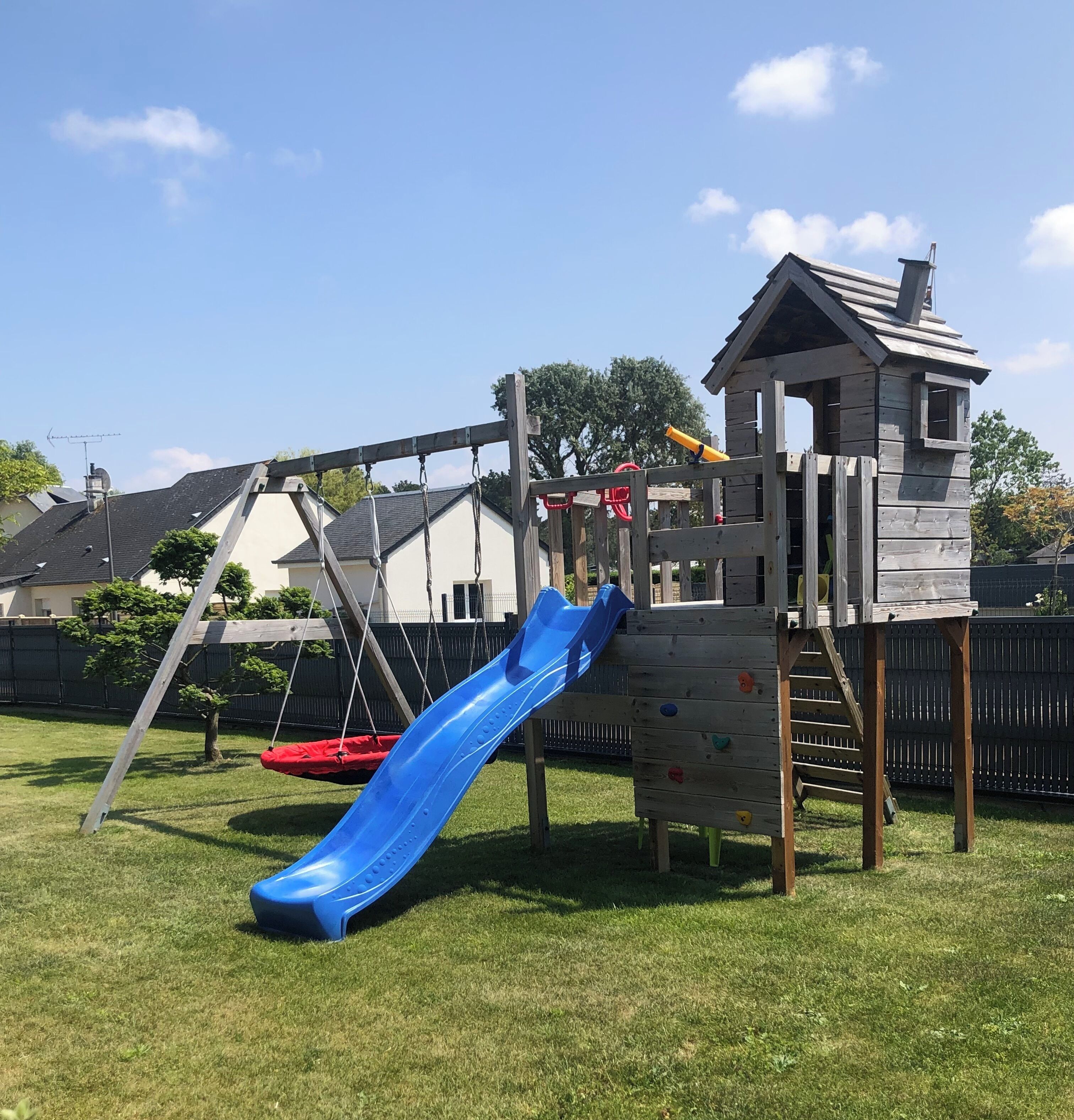 Une aire de jeux en bois avec un toboggan bleu et un mur d’escalade.