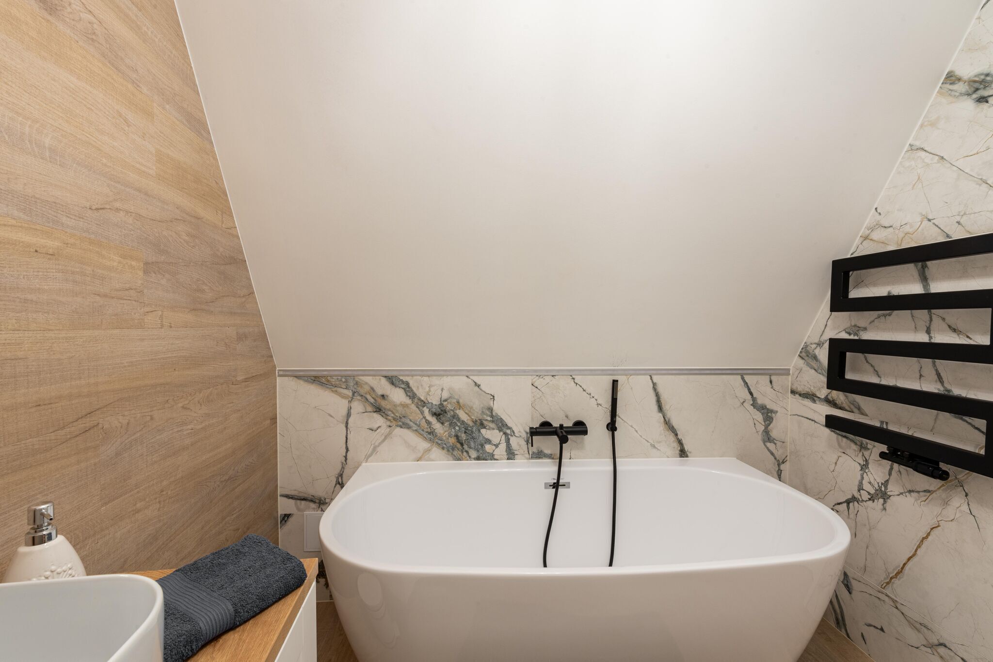 Une salle de bain moderne avec une baignoire sur pieds, un meuble-lavabo en bois et un mur en marbre.