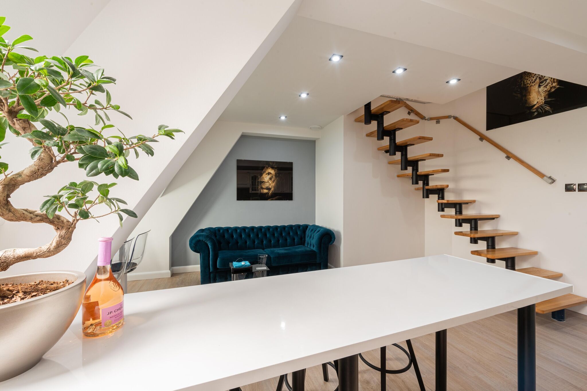 A modern interior with a white table, a potted plant, a blue sofa, and a staircase with wooden steps.