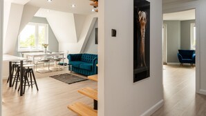 A modern living room with a dining area, a teal sofa, and a mounted giraffe sculpture.