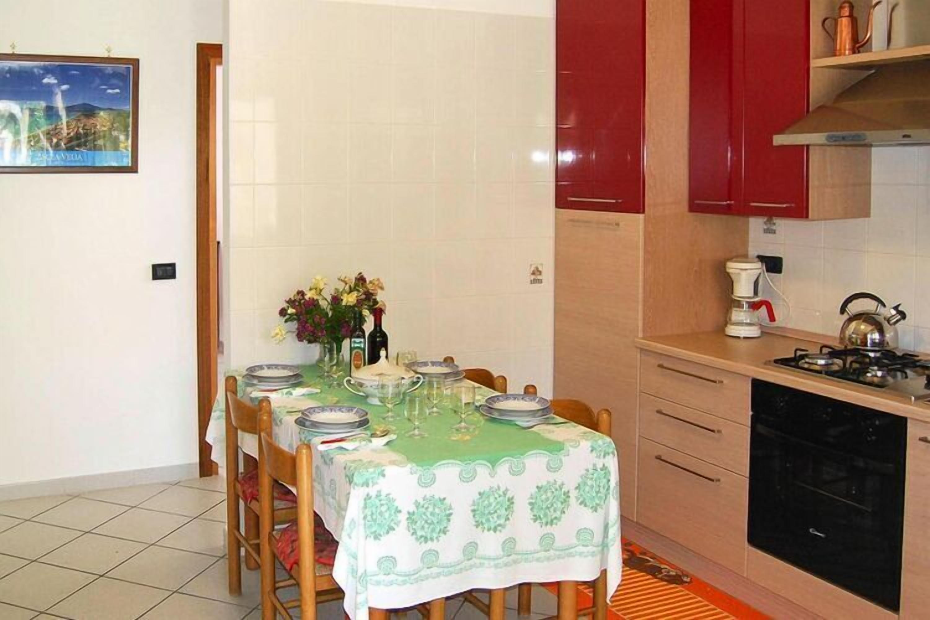 A dining area with a table set for four, a kitchen with red cabinets, and a tiled backsplash.