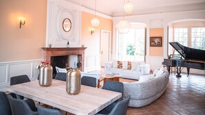 Een ruime woonkamer met een open haard, een piano en een eethoek met een tafel en stoelen.