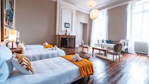 Een hotelkamer met twee bedden, een open haard, een eettafel en een groot raam.