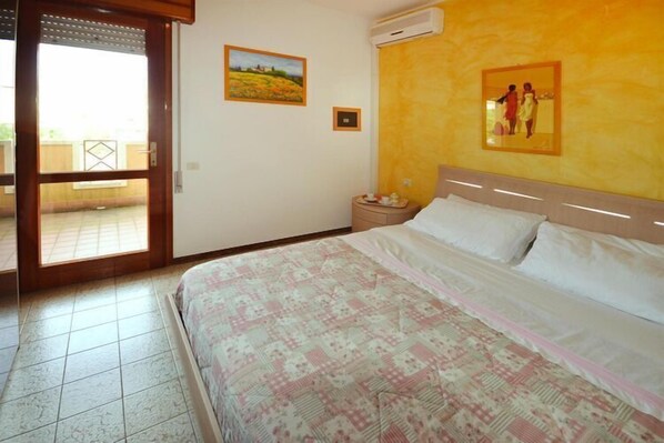 A bedroom with a bed, a nightstand, a wall-mounted air conditioner, and a sliding glass door leading to an outdoor area.