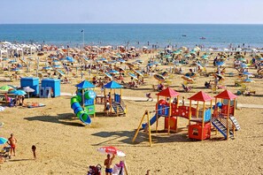 Una playa concurrida con numerosos paraguas, una zona de juegos infantiles y una vista despejada al mar.