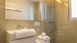A modern bathroom with a white vanity, a glass shower enclosure, and a large mirror. - Nest Wehntalerstrasse (Zürich)