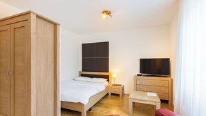 A bedroom with a bed, wooden wardrobe, bedside table, TV, and a red sofa. - Nest Wehntalerstrasse (Zürich)