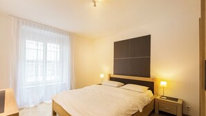 A neatly arranged bedroom with a large bed, bedside lamps, and a window with sheer curtains. - Nest Wehntalerstrasse (Zürich)