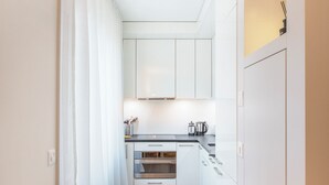 A narrow hallway leading to a kitchen with white cabinets, a countertop, and a coffee maker. - Nest Wehntalerstrasse (Zürich)