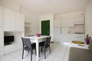 A modern kitchen with white cabinets, a dining table with chairs, a green door, and a small plant.