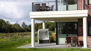 Un edificio moderno de dos pisos con un balcón que tiene asientos al aire libre y una parrilla.