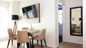 Un comedor moderno con una mesa redonda, seis sillas, un televisor de pantalla plana montado en la pared y un espejo grande en la pared contigua.