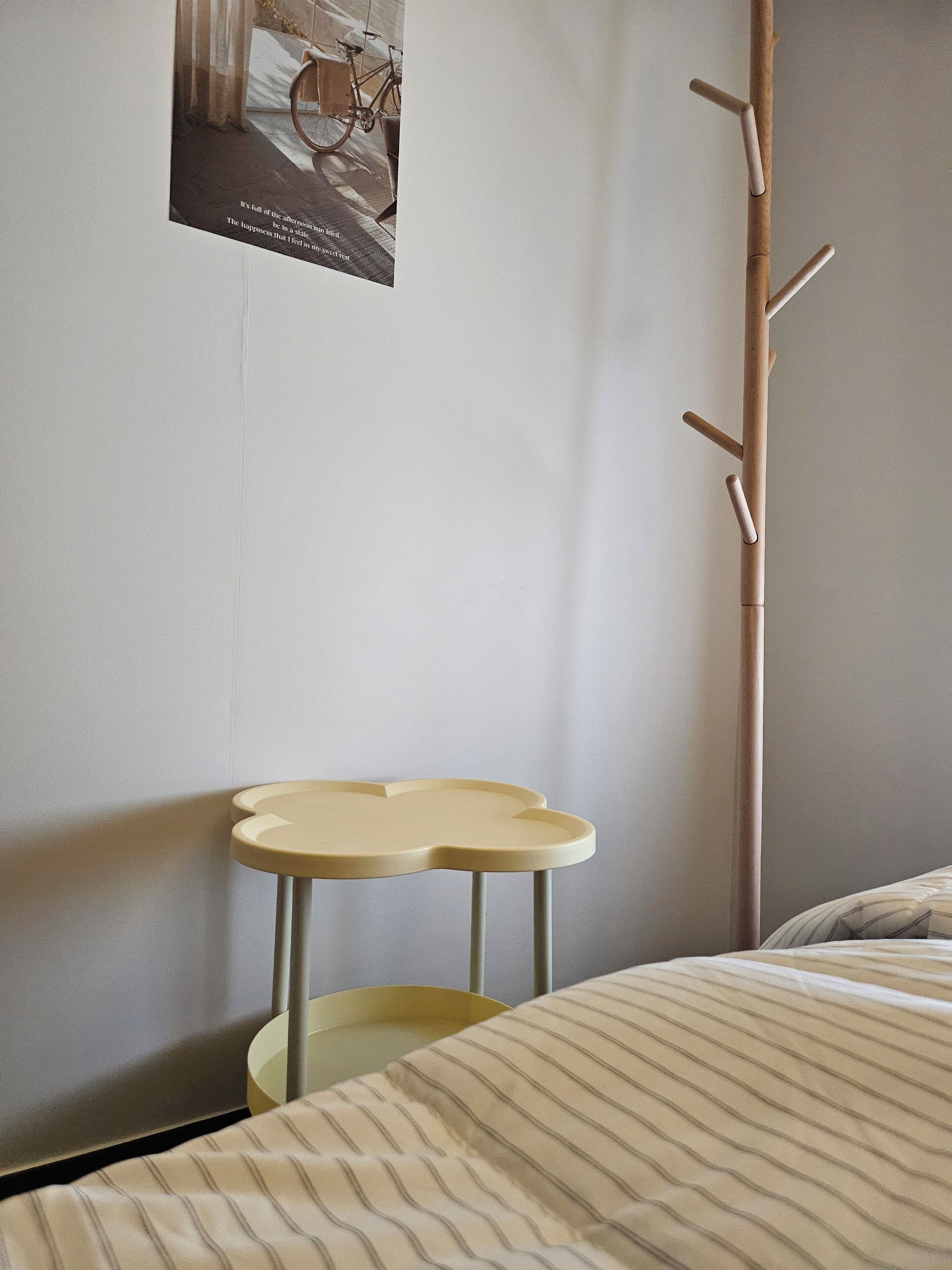 A corner of a room with a bed, a small round table, and a coat rack.