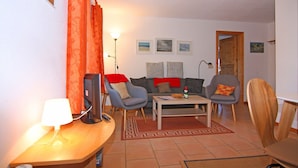A living room with a sofa, two armchairs, a coffee table, a lamp, and a TV.