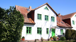 A two-story house with a white exterior and green window frames, a tiled roof, and a small front garden with potted plants.