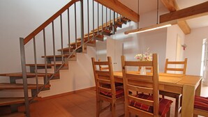 Eine Treppe mit Holzbalken und Metallgeländern, ein Esstisch aus Holz mit Stühlen und eine Vase mit Blumen.