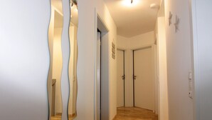 Un pasillo con suelo de madera, paredes blancas y una puerta al final.