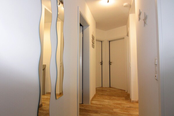 A hallway with wooden flooring, white walls, and a door at the end.