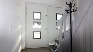 Una puerta blanca con tres ventanas, un perchero y una escalera con barandilla.