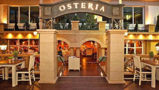 Hotellin aula, jonka keskellä on suuri holvikaari, jossa lukee ”OSTERIA”. Aulassa on baarialue istumapaikkoineen ja sieltä on näkymä hotellin sisätiloihin.