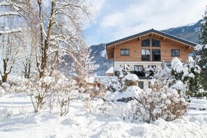 Una baita di legno con ampie finestre, circondata da alberi innevati e montagne sullo sfondo.
