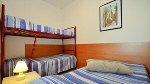 Una cama individual con ropa de cama a rayas, una lámpara de noche y un cuadro en la pared.