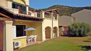 A two-story building with a covered patio area, outdoor seating, and a view of a hillside. - Apartment in Villaputzu with garden (Chia)