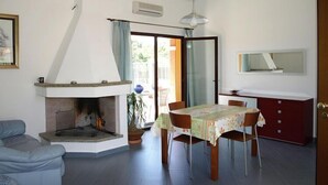 A dining area with a table set for four, a fireplace, a sofa, and a sliding glass door leading to an outdoor area. - Apartment in Villaputzu with garden (Chia)