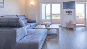 A modern living room with a grey sofa, a wooden coffee table, and a TV mounted on the wall. - Exklusiv eingerichtetes Ferienhaus in Strandnähe (Dagebüll)