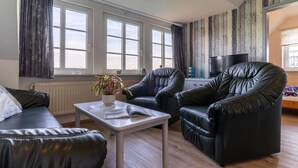 A living room with a sofa, two armchairs, a coffee table, a TV, and a window with curtains.