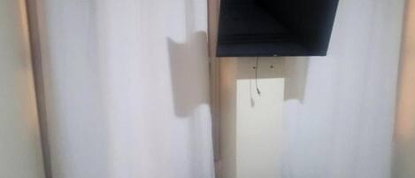 A room with a mounted flat-screen TV on the wall and a small black table in the corner.