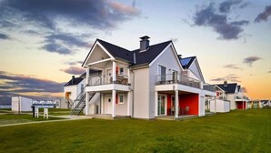 Een modern herenhuis met twee verdiepingen, een balkon en een overdekte veranda, met een keurig onderhouden gazon.
