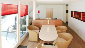 A modern dining area with a central table and four chairs, a wooden counter, and a red lamp.