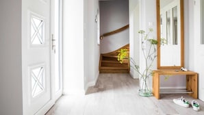 Ein Flur mit weißen Türen, einer Holztreppe, einem Spiegel und einer Vase mit Blumen.