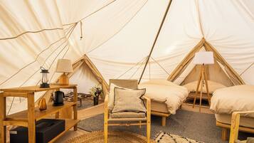 A tented accommodation with a wooden table, a chair, and two beds.