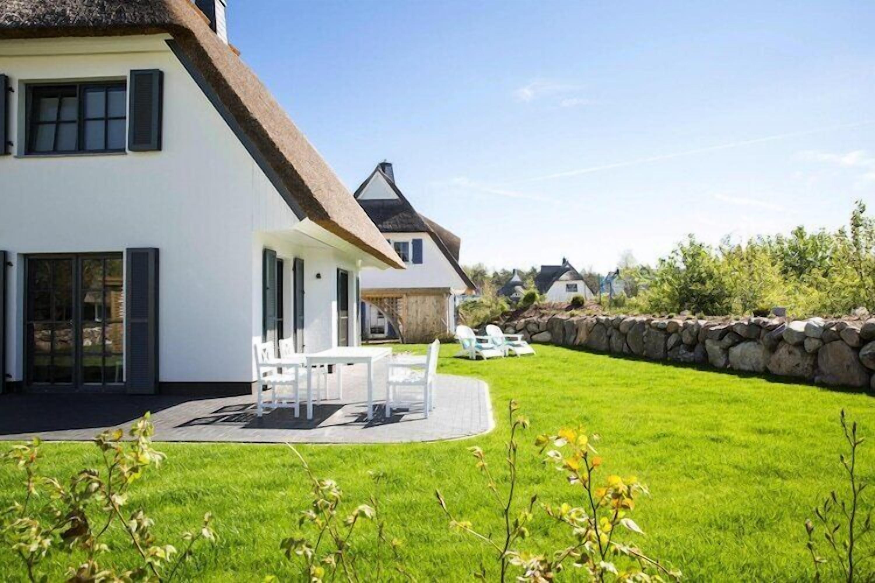 A modern house with a white exterior and a thatched roof, a patio with outdoor furniture, and a well-maintained lawn.