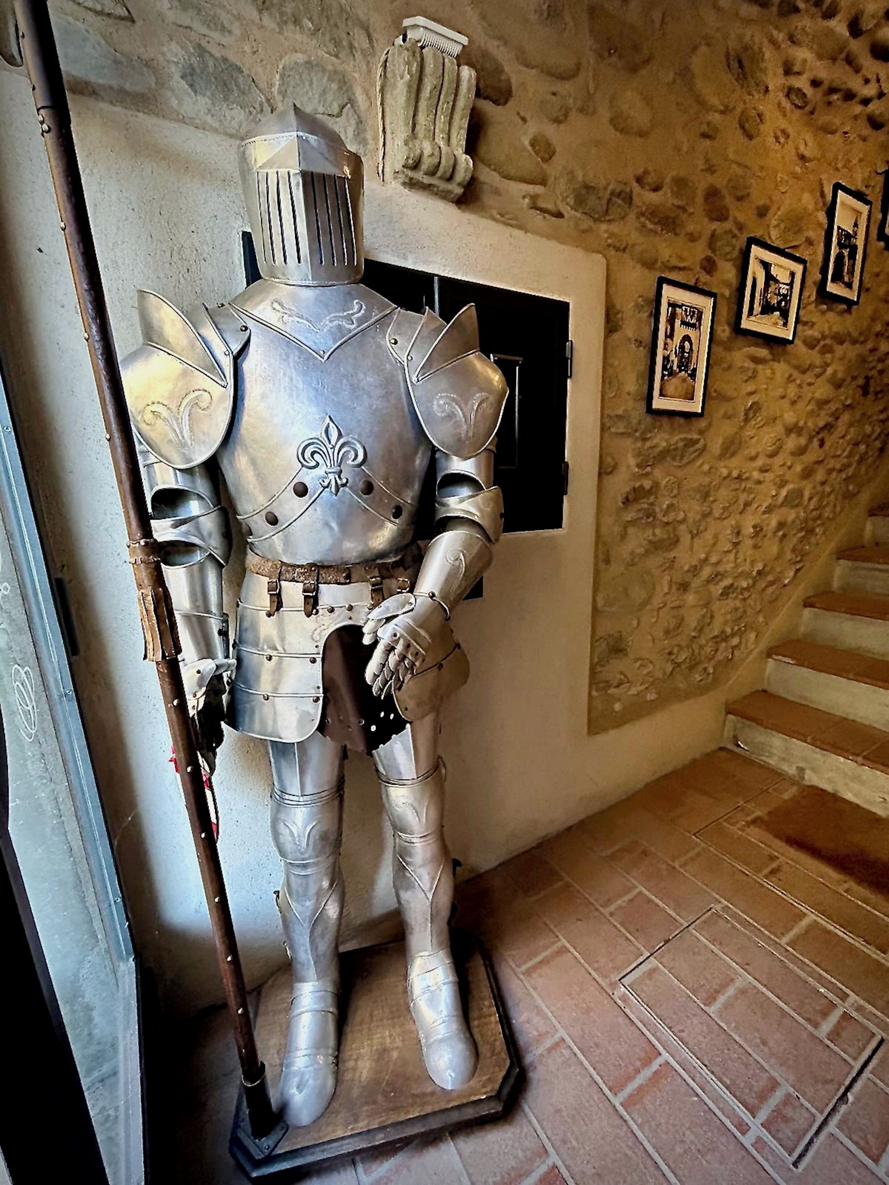 Un traje de armadura histórica expuesto en una sala con paredes de piedra y suelo de baldosas.
