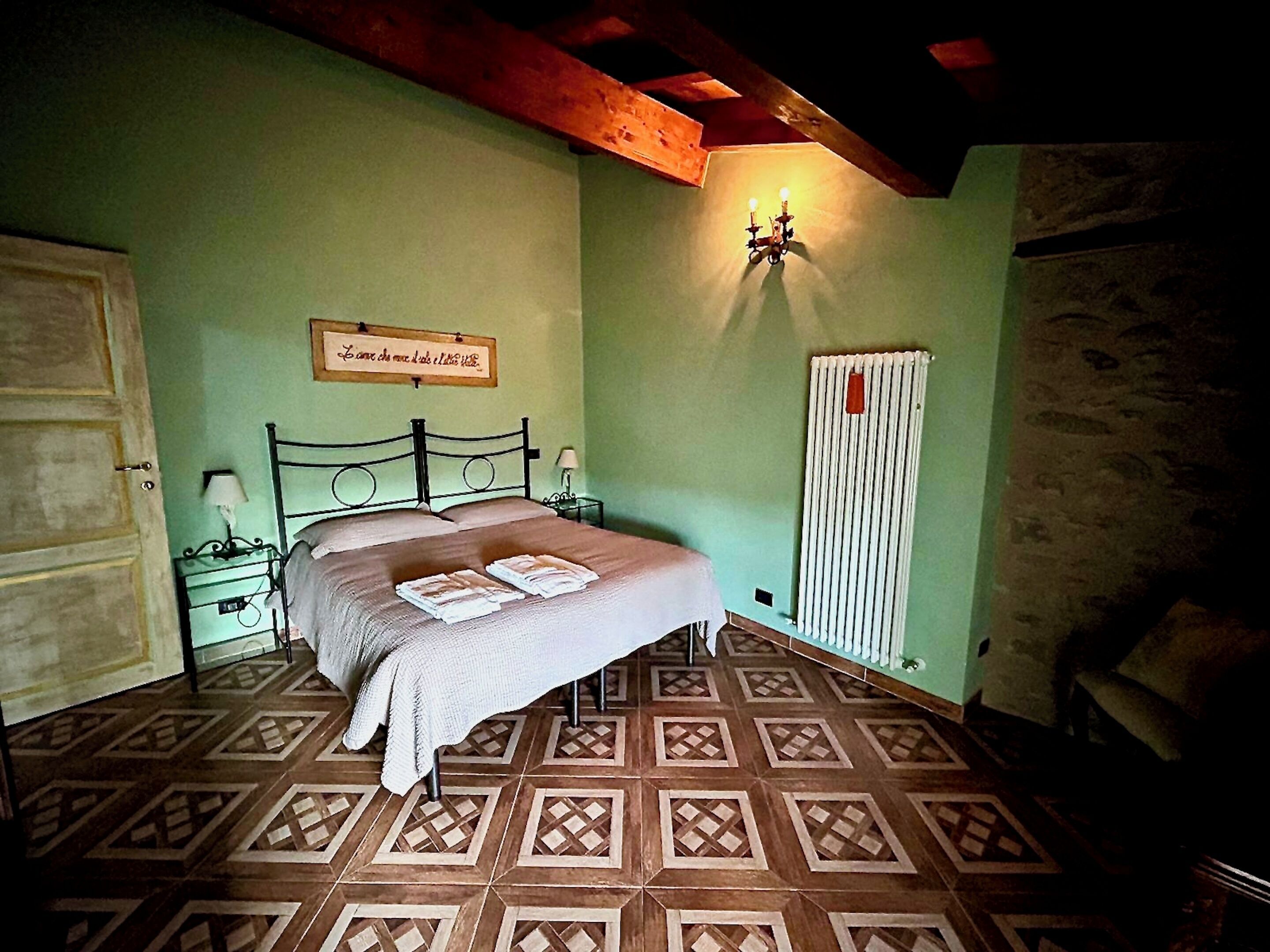 A bedroom with a bed, a nightstand, a wall-mounted lamp, a radiator, and a patterned floor.