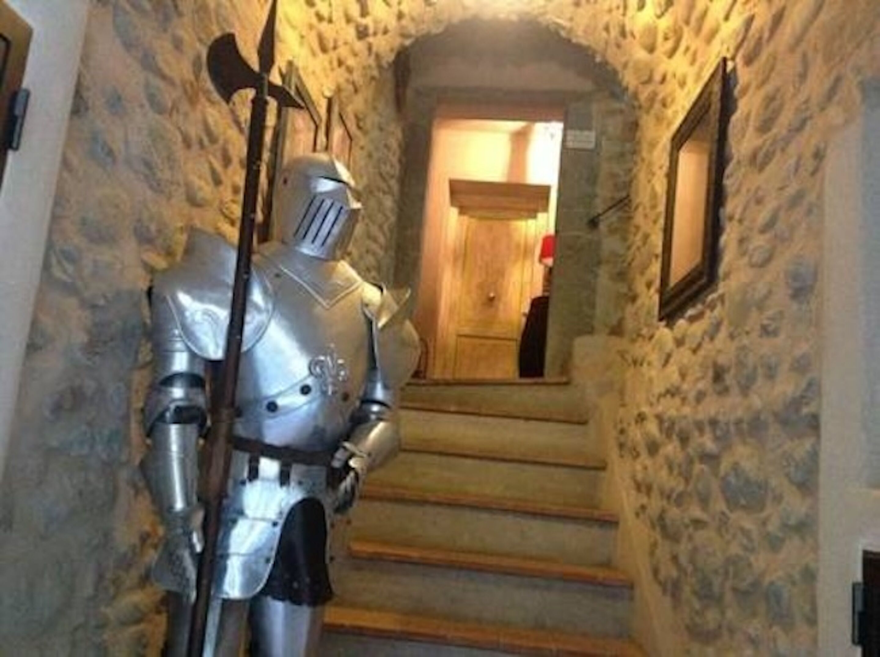 Una estatua de un caballero medieval en un pasillo de paredes de piedra con una puerta de madera al final de una escalera.
