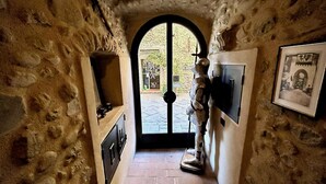 Un étroit couloir en pierre, avec une statue au bout, une porte donnant sur l’extérieur et un tableau encadré accroché au mur.