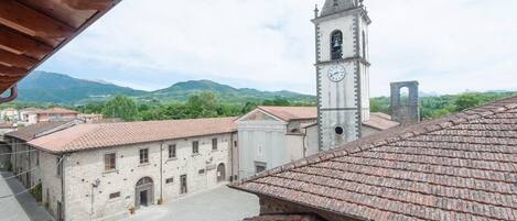 Um edifício histórico com torre do relógio, rodeado por arquitetura tradicional e uma paisagem montanhosa ao fundo.
