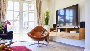 Un salón moderno con un televisor de pantalla plana grande, un sillón de cuero marrón, una mesa de centro de vidrio y una alfombra roja.