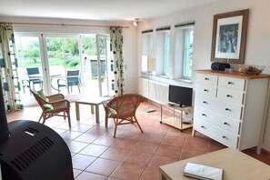 Ein Zimmer mit Fernseher, Tisch, Stühlen, Grill und Fenster mit Blick ins Freie.