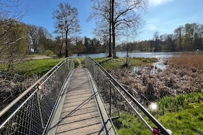 A wooden boardwalk with metal railings, leading to a body of water surrounded by trees and grass.