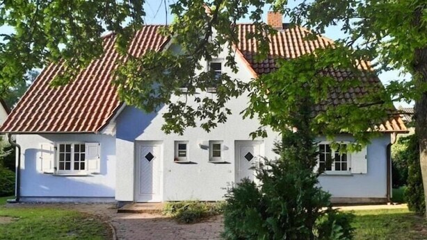 Un bâtiment blanc avec un toit recouvert de tuiles et un chemin en briques menant à l’entrée.