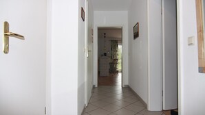 Un couloir aux murs blancs, doté d’un sol carrelé et d’une porte ornée d’une poignée dorée.