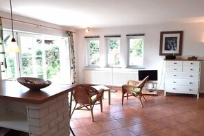 A spacious room with a dining area, two wicker chairs, a white cabinet, and a television.