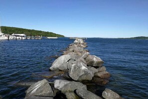 Kivinen laituri, joka ulottuu tyyniin veteen. Vasemmalla puolella on laivoja ja kauempana näkyy silta.