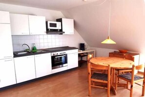 A compact kitchen with white cabinets, a microwave, a stove, and a dining table with chairs.