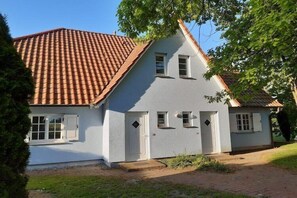Ein zweigeschossiges Haus mit rotem Ziegeldach, weißen Außenwänden und einem Hauseingang mit Tür und Fenstern.